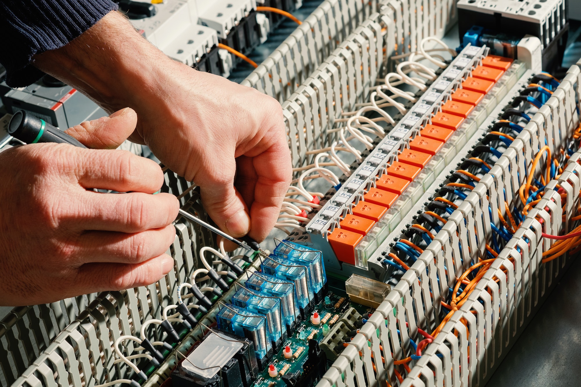 Electrical installation works. Worker's hands on the background of the circuit board.